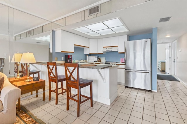 kitchen featuring kitchen peninsula, light tile patterned floors, a breakfast bar area, white cabinetry, and stainless steel refrigerator