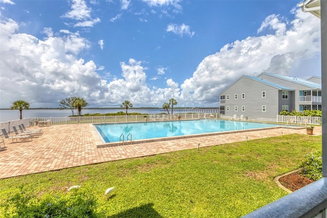 view of swimming pool featuring a lawn, a patio area, and a water view