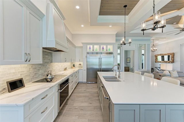 kitchen featuring appliances with stainless steel finishes, custom exhaust hood, a spacious island, sink, and decorative light fixtures