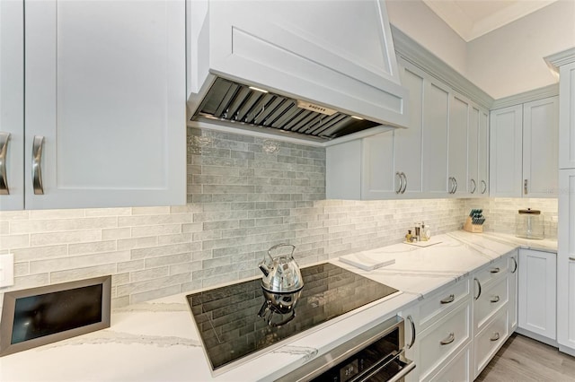 kitchen featuring premium range hood, light stone counters, tasteful backsplash, black electric cooktop, and white cabinets