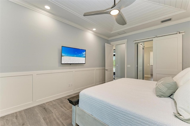 bedroom with a raised ceiling, crown molding, ceiling fan, a barn door, and light hardwood / wood-style floors