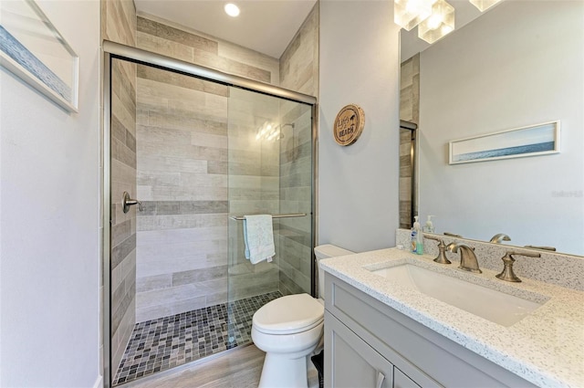 bathroom featuring hardwood / wood-style flooring, vanity, a shower with shower door, and toilet