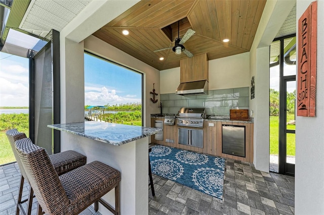 kitchen with wooden ceiling, decorative backsplash, range hood, fridge, and a kitchen bar