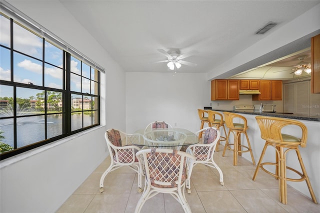 tiled dining space with ceiling fan and a water view