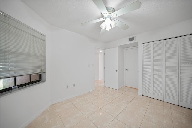 unfurnished bedroom with light tile patterned floors, a textured ceiling, a closet, and ceiling fan