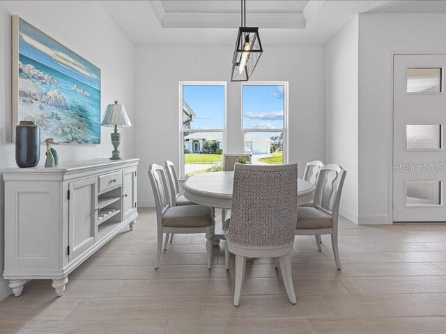 dining room featuring a raised ceiling, crown molding, light wood-style flooring, and baseboards