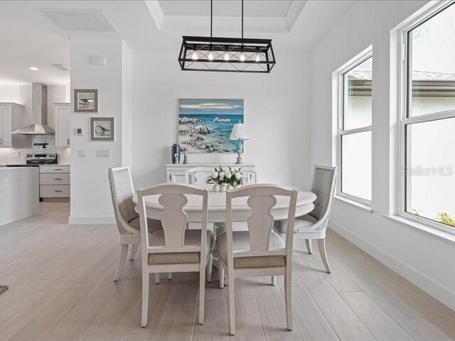 dining room with ornamental molding, light wood-type flooring, visible vents, and baseboards