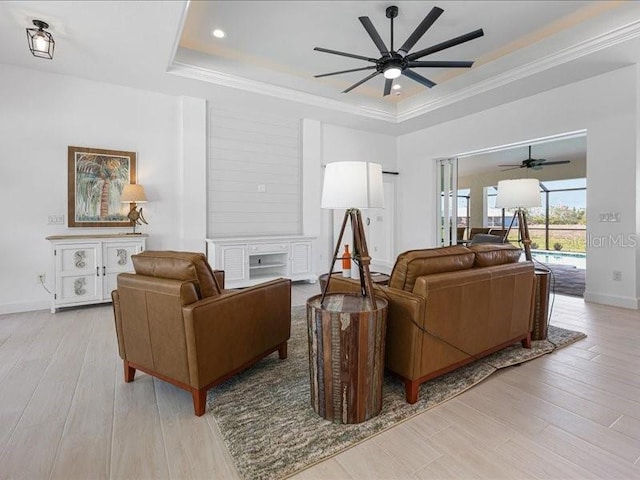 living room featuring light wood-type flooring, a tray ceiling, and crown molding