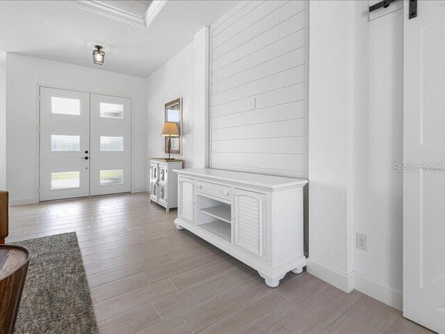 foyer with a barn door, baseboards, wood finished floors, crown molding, and french doors