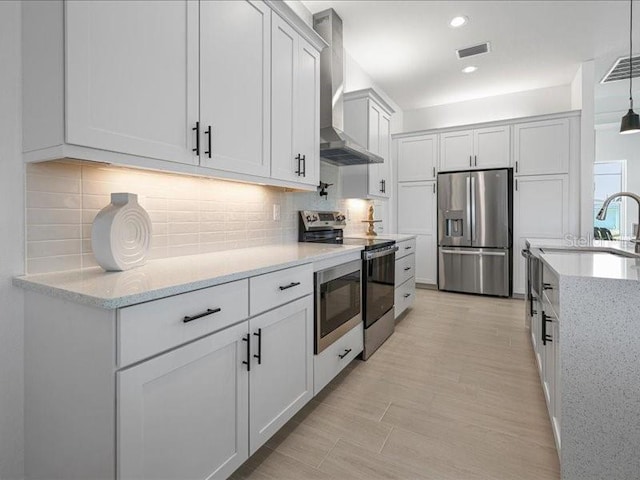 kitchen featuring light stone counters, decorative backsplash, appliances with stainless steel finishes, a sink, and wall chimney range hood