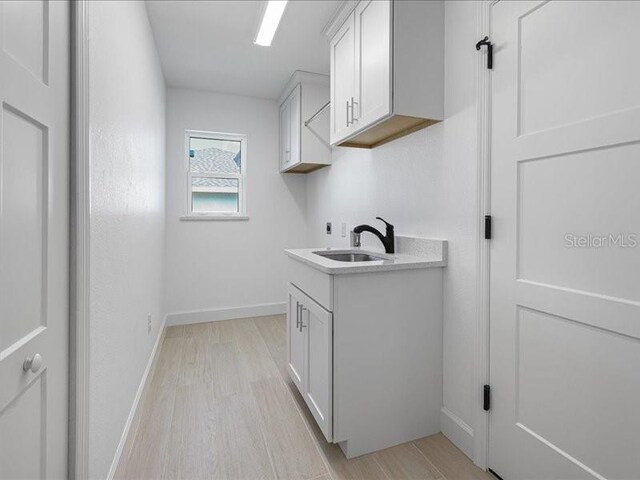 clothes washing area with light wood-style floors, cabinet space, a sink, and baseboards