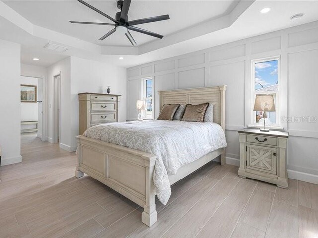 bedroom featuring a tray ceiling, wood finish floors, visible vents, a decorative wall, and baseboards