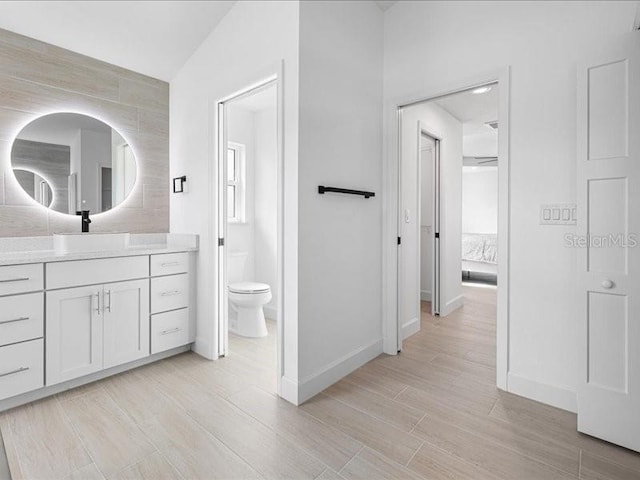 ensuite bathroom featuring wood finish floors, baseboards, vanity, and toilet