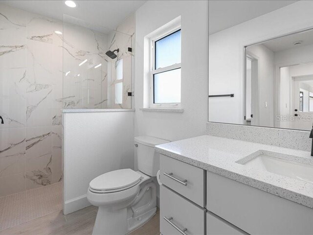 full bathroom featuring toilet, vanity, a marble finish shower, and wood finished floors