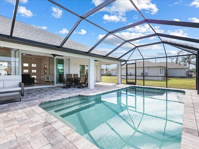 pool featuring a ceiling fan, glass enclosure, a patio area, and a lawn