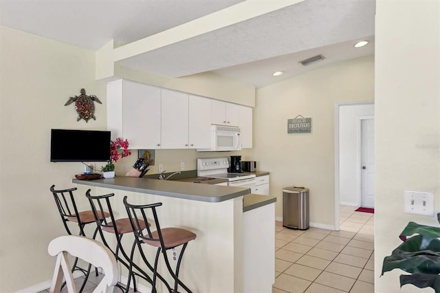 kitchen with lofted ceiling, a breakfast bar, kitchen peninsula, white appliances, and white cabinets