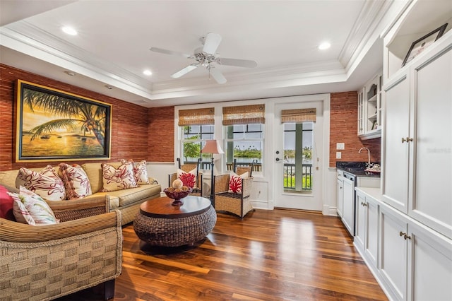 living room with a raised ceiling, crown molding, dark wood-type flooring, and ceiling fan