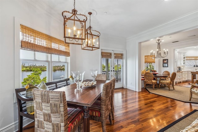 dining area featuring dark hardwood / wood-style flooring, crown molding, a water view, an inviting chandelier, and french doors