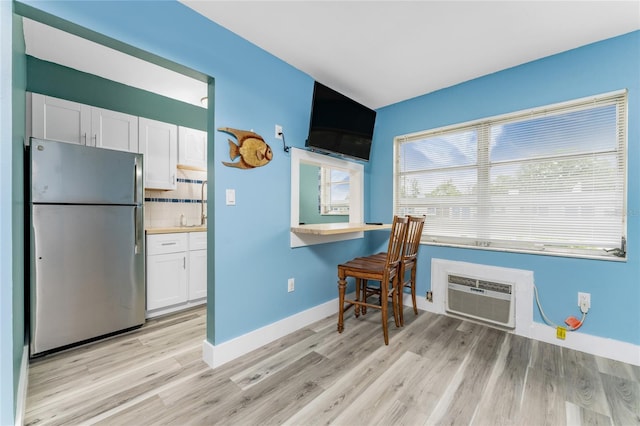 kitchen featuring stainless steel refrigerator, light hardwood / wood-style flooring, a wall mounted AC, decorative backsplash, and white cabinets