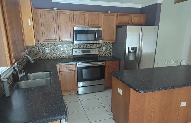 kitchen featuring crown molding, appliances with stainless steel finishes, tasteful backsplash, light tile patterned floors, and sink