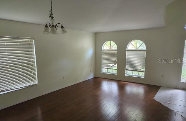 empty room with dark hardwood / wood-style flooring and a notable chandelier