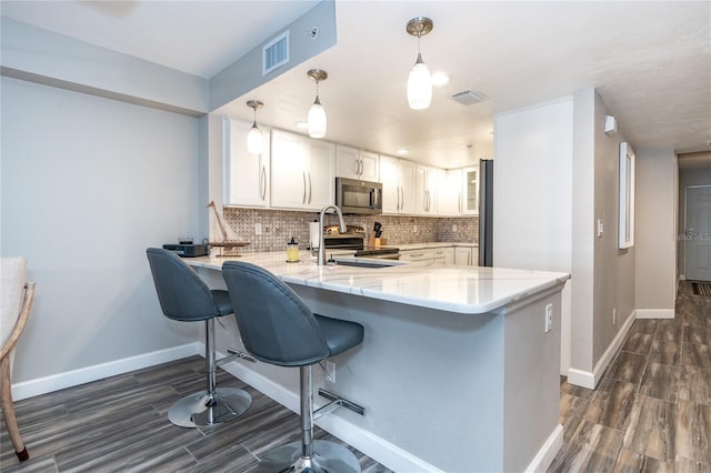 kitchen featuring kitchen peninsula, white cabinets, stainless steel appliances, pendant lighting, and a kitchen breakfast bar