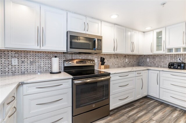 kitchen with appliances with stainless steel finishes, dark hardwood / wood-style flooring, white cabinets, and backsplash