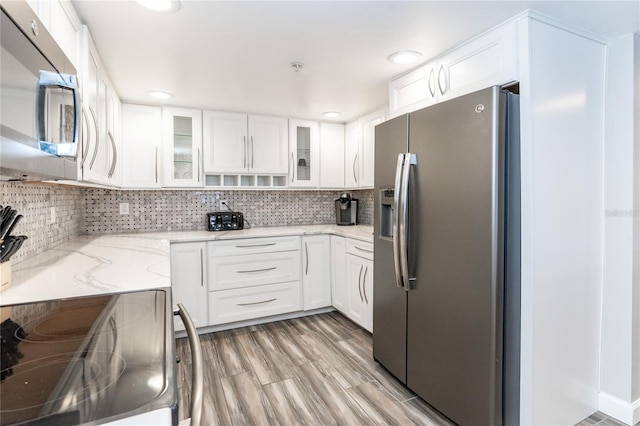 kitchen with appliances with stainless steel finishes, light wood-type flooring, tasteful backsplash, and white cabinetry