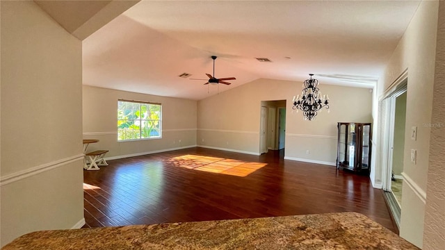 spare room with ceiling fan with notable chandelier, vaulted ceiling, and dark wood-type flooring