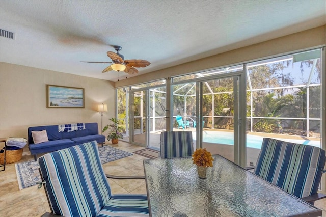 interior space featuring a textured ceiling, light tile patterned floors, a sunroom, visible vents, and a ceiling fan