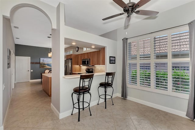 kitchen with hanging light fixtures, light tile patterned floors, kitchen peninsula, stainless steel appliances, and decorative backsplash