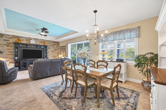 tiled dining space with ceiling fan with notable chandelier and a raised ceiling