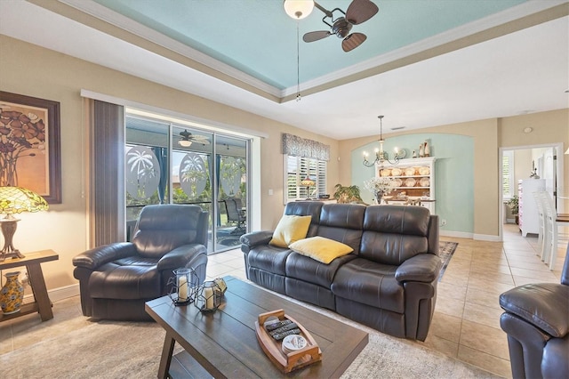 tiled living room with crown molding, ceiling fan with notable chandelier, and a raised ceiling