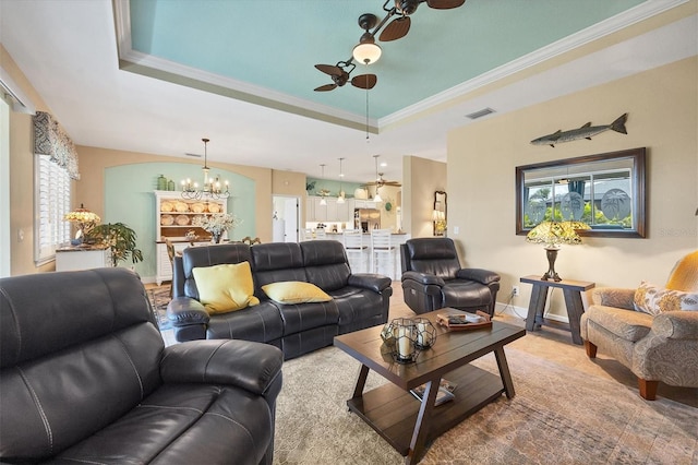 living room featuring ceiling fan with notable chandelier, a tray ceiling, and crown molding