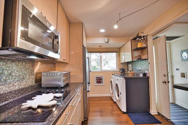 kitchen with washer and dryer, appliances with stainless steel finishes, light brown cabinetry, decorative backsplash, and hardwood / wood-style flooring