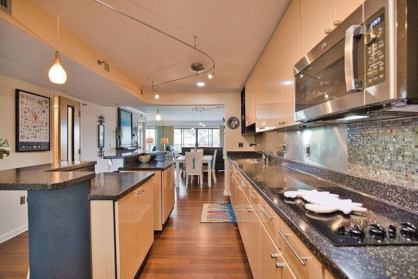 kitchen with light brown cabinetry, pendant lighting, black gas stovetop, dark hardwood / wood-style floors, and dark stone countertops