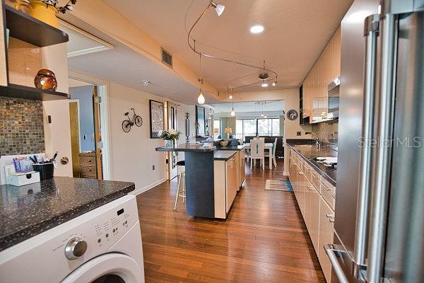 kitchen featuring high end fridge, dark hardwood / wood-style flooring, decorative backsplash, washer / dryer, and a breakfast bar area