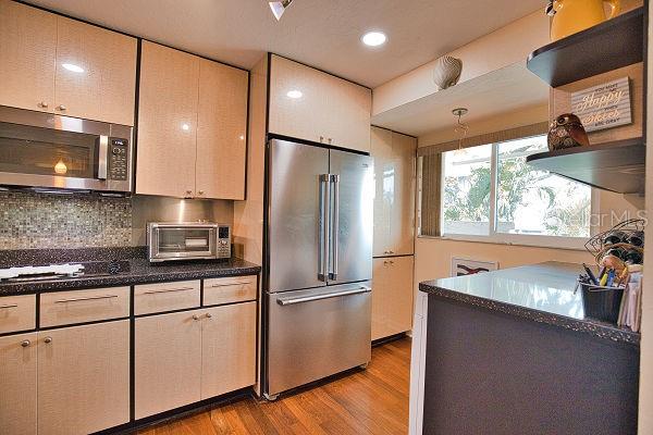 kitchen with dark stone counters, stainless steel appliances, pendant lighting, backsplash, and light wood-type flooring