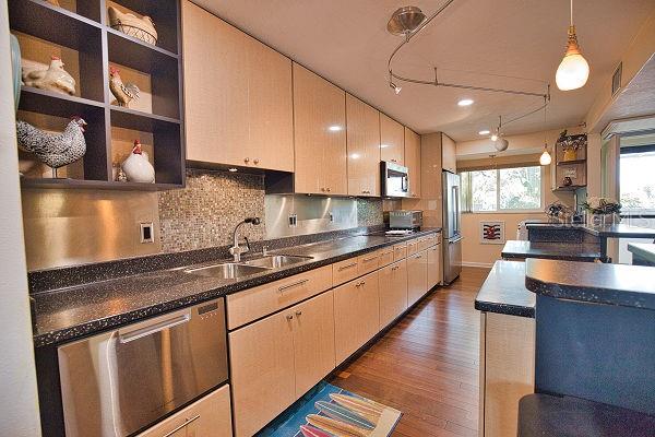 kitchen with stainless steel appliances, hanging light fixtures, sink, backsplash, and dark wood-type flooring