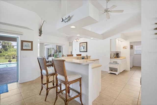 kitchen with ceiling fan with notable chandelier, lofted ceiling, a kitchen bar, white cabinetry, and light tile patterned flooring