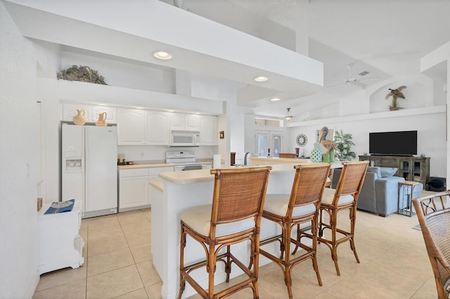 kitchen featuring white appliances, white cabinets, a towering ceiling, a kitchen breakfast bar, and ceiling fan