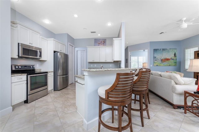 kitchen with white cabinetry, a kitchen bar, ceiling fan, light stone countertops, and appliances with stainless steel finishes