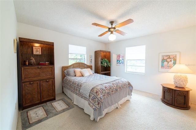 bedroom featuring light colored carpet, a textured ceiling, and ceiling fan