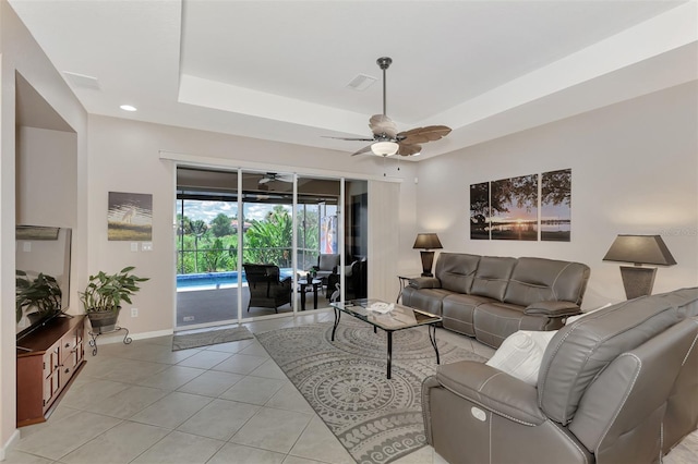 tiled living room with ceiling fan and a raised ceiling