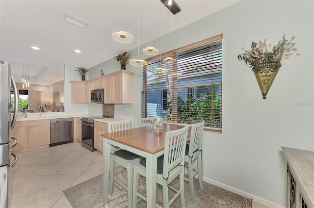 kitchen with light tile patterned floors, appliances with stainless steel finishes, light brown cabinetry, and hanging light fixtures