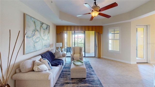 living room with a raised ceiling, light tile patterned floors, and ceiling fan