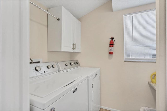 clothes washing area featuring cabinets, plenty of natural light, washing machine and dryer, and a textured ceiling