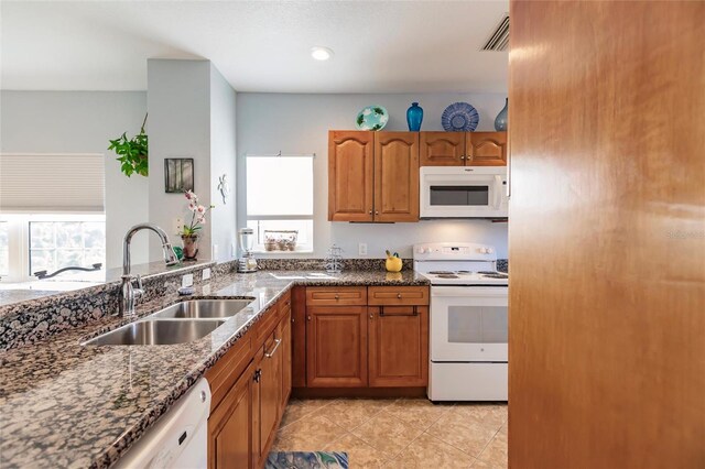 kitchen with dark stone counters, light tile patterned floors, white appliances, and sink