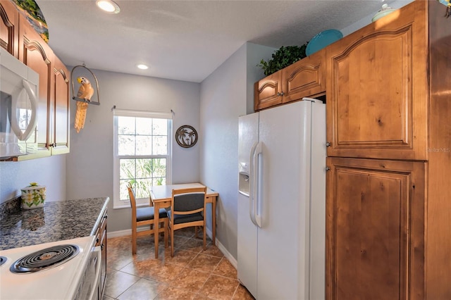 kitchen with dark stone counters, light tile patterned floors, and white appliances