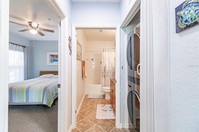 interior space featuring ceiling fan, stacked washing maching and dryer, shower / bath combination with curtain, toilet, and tile patterned flooring